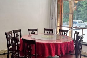 Una mesa redonda con cubierta de vidrio y mantel rojo, rodeada de sillas de madera, en una habitación con un ventanal grande.