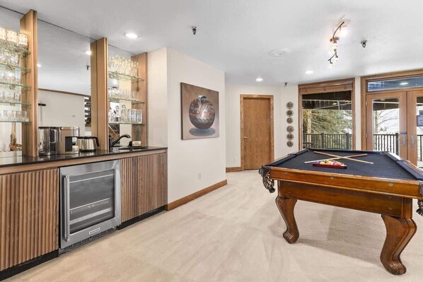 A pool table, a bar area with glassware, and a door leading to a balcony.