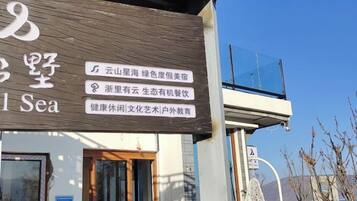 A building with a signboard displaying text in multiple languages, a clear sky, and a view of the sea.