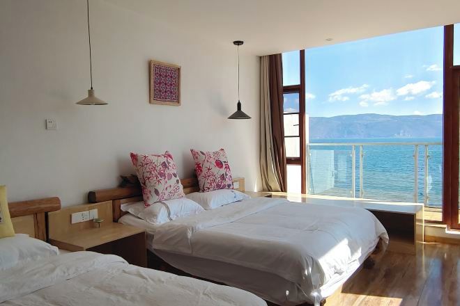 Une chambre avec deux lits, une grande fenêtre donnant sur la mer et un plancher en bois.