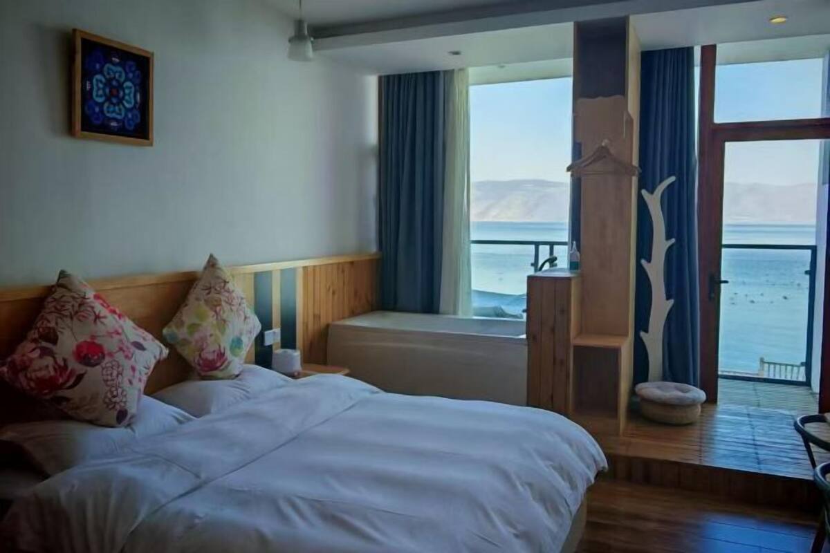 Une chambre à coucher avec un lit, une fenêtre avec des rideaux, une vue sur la mer et un banc en bois.