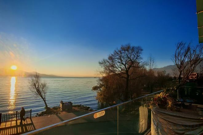 A waterfront view with a sunset, a wooden deck, and a railing.