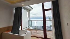 A bathroom with a bathtub, a sink, and a large window overlooking a balcony with a view of the sea. - HillSea Green Holiday Inn , Dali (Dali City)