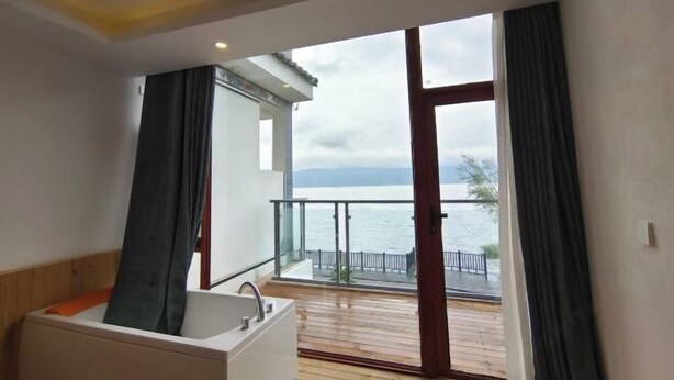 A bathroom with a bathtub, a sink, and a large window overlooking a balcony with a view of the sea. - HillSea Green Holiday Inn , Dali (Dali City)