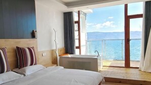A hotel room with a large bed, a bathtub, and a balcony with a view of the sea. - HillSea Green Holiday Inn , Dali (Dali City)