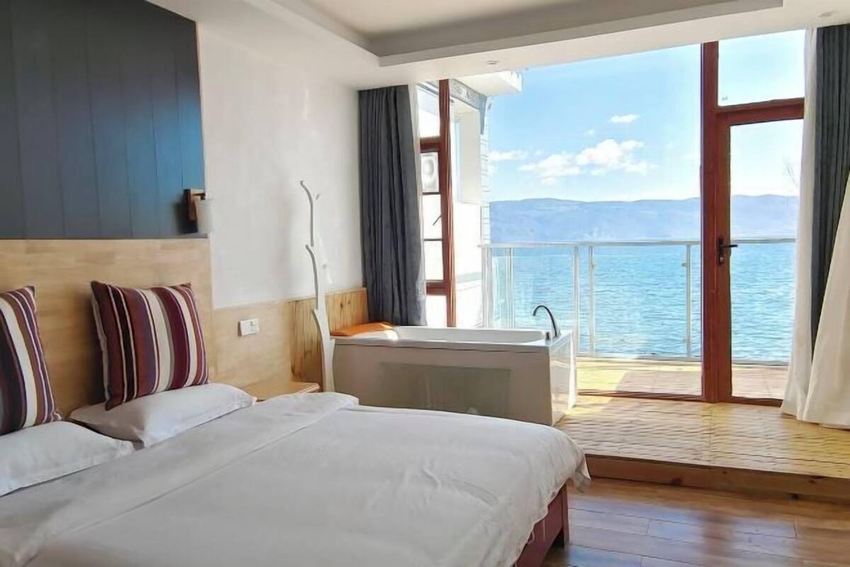 Une chambre d’hôtel avec un grand lit, une baignoire et un balcon donnant sur la mer.