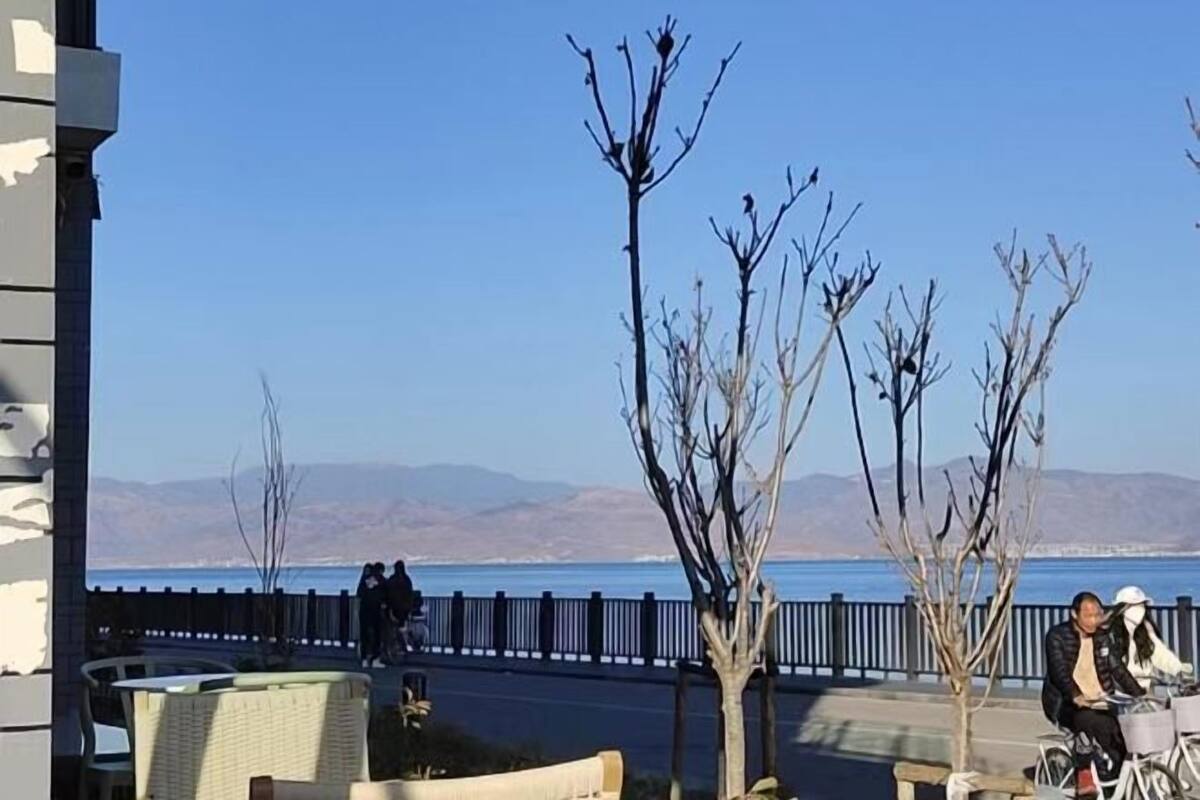Une vue sur la côte, avec un ciel dégagé, une clôture en bois et quelques personnes près de l’eau.