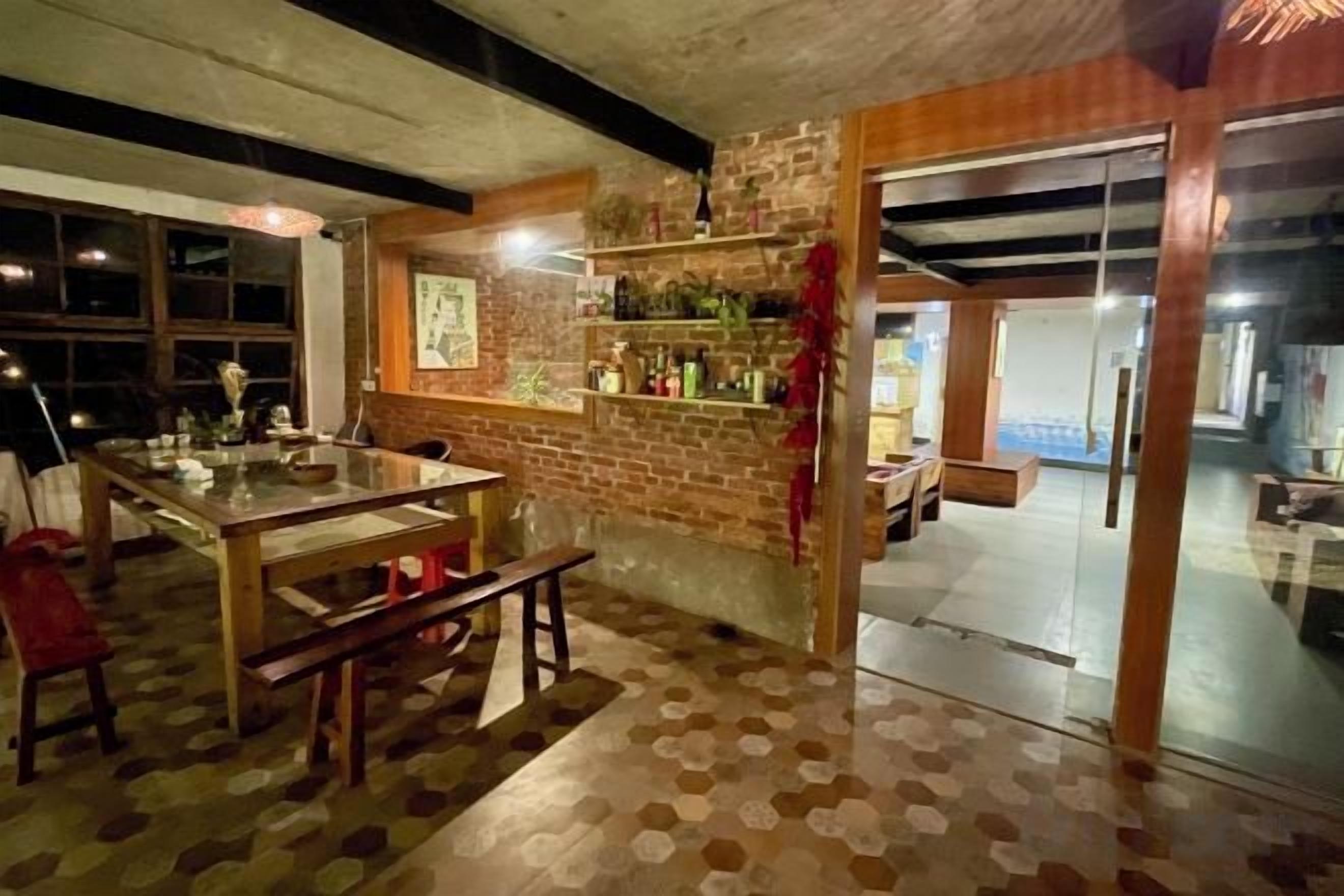 A room with a dining table, benches, a brick wall, and a glass door leading to another area.