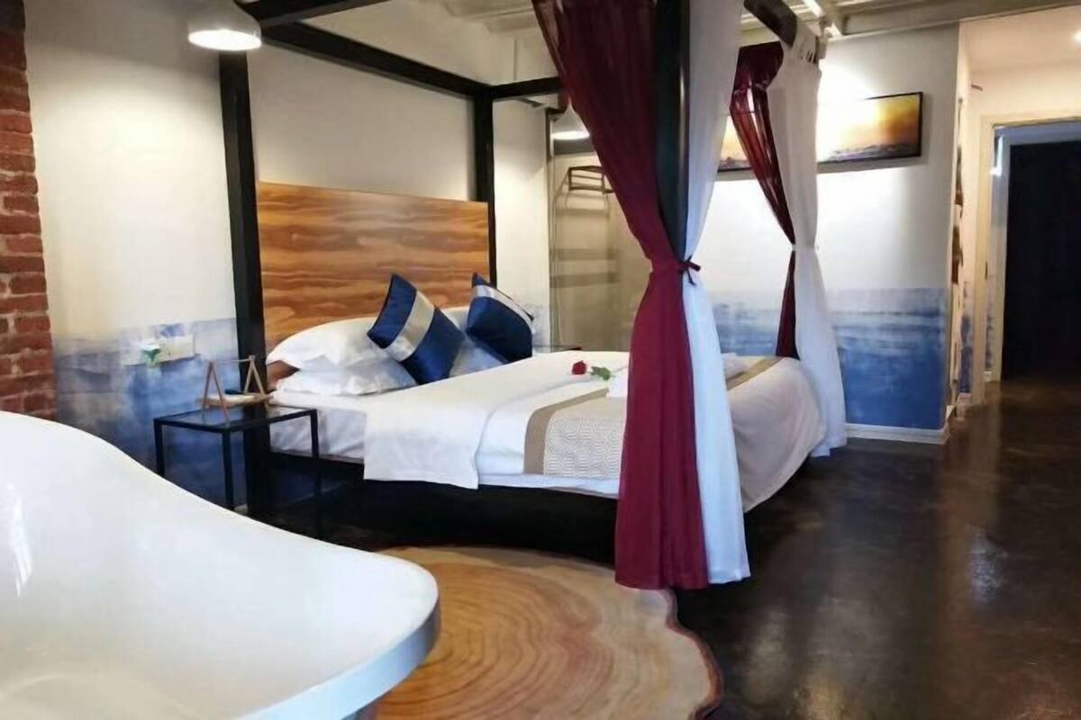 A modern hotel room with a curved bathtub, a wooden headboard, and a bed with white bedding and blue pillows.