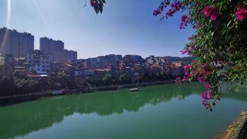 A river with buildings in the background, a bridge, and pink flowers in the foreground.