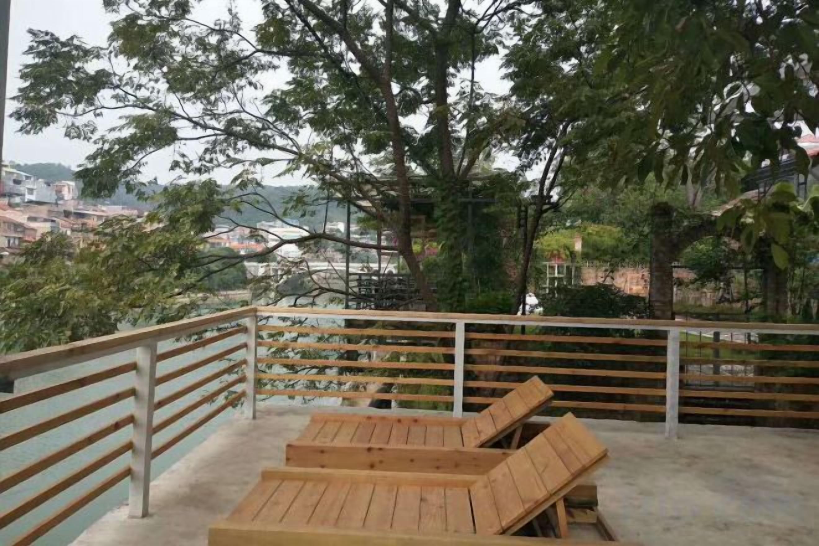 Un balcón con sillones de madera y barandilla de metal con vistas a un paisaje urbano.