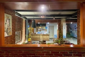 A room with a brick wall, wooden ceiling beams, a wooden counter, and a door leading to another room. - Goose city story (Baise)