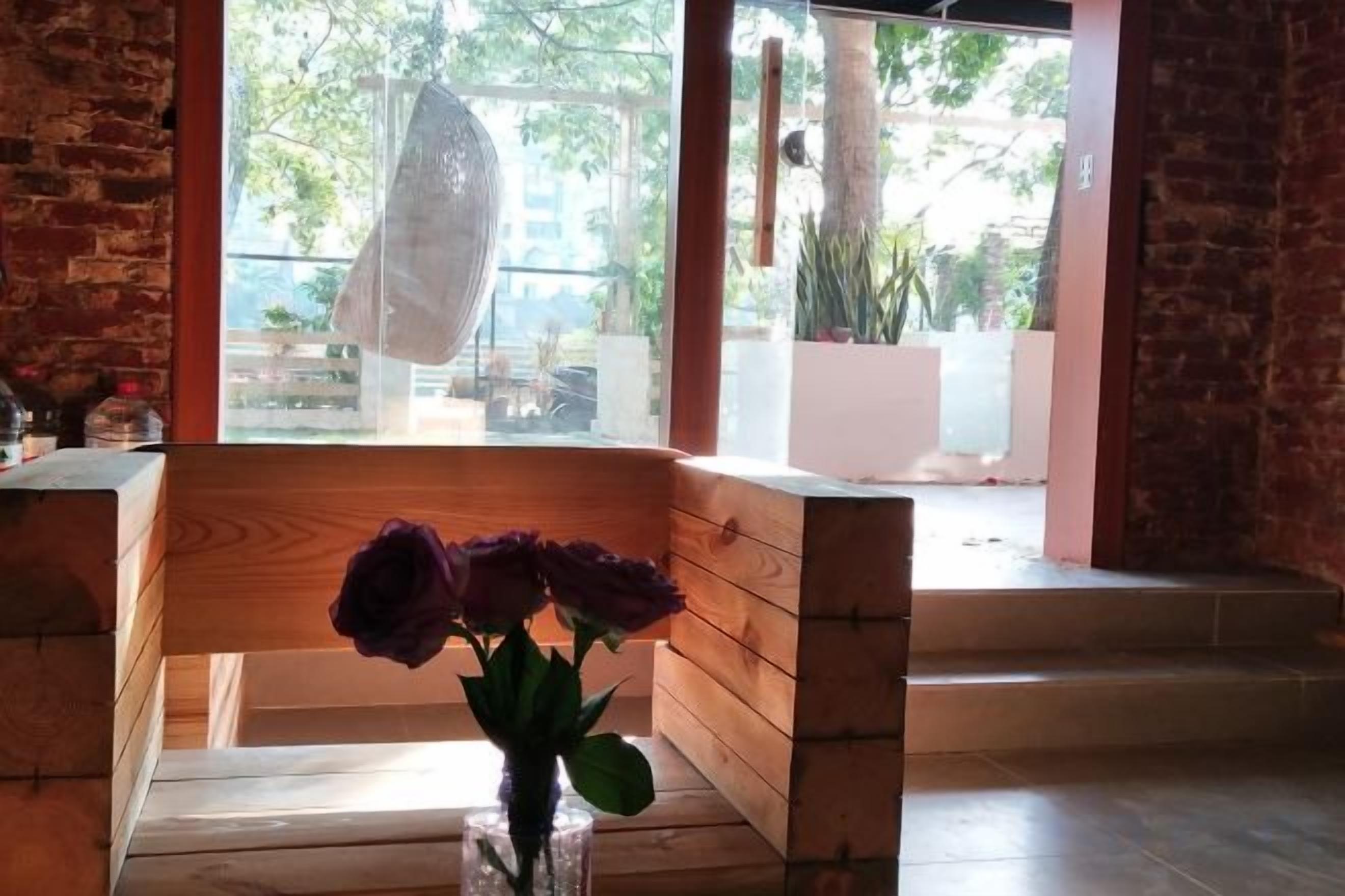 A wooden bench with a vase of purple flowers, a brick wall, and a view of an outdoor area with plants.