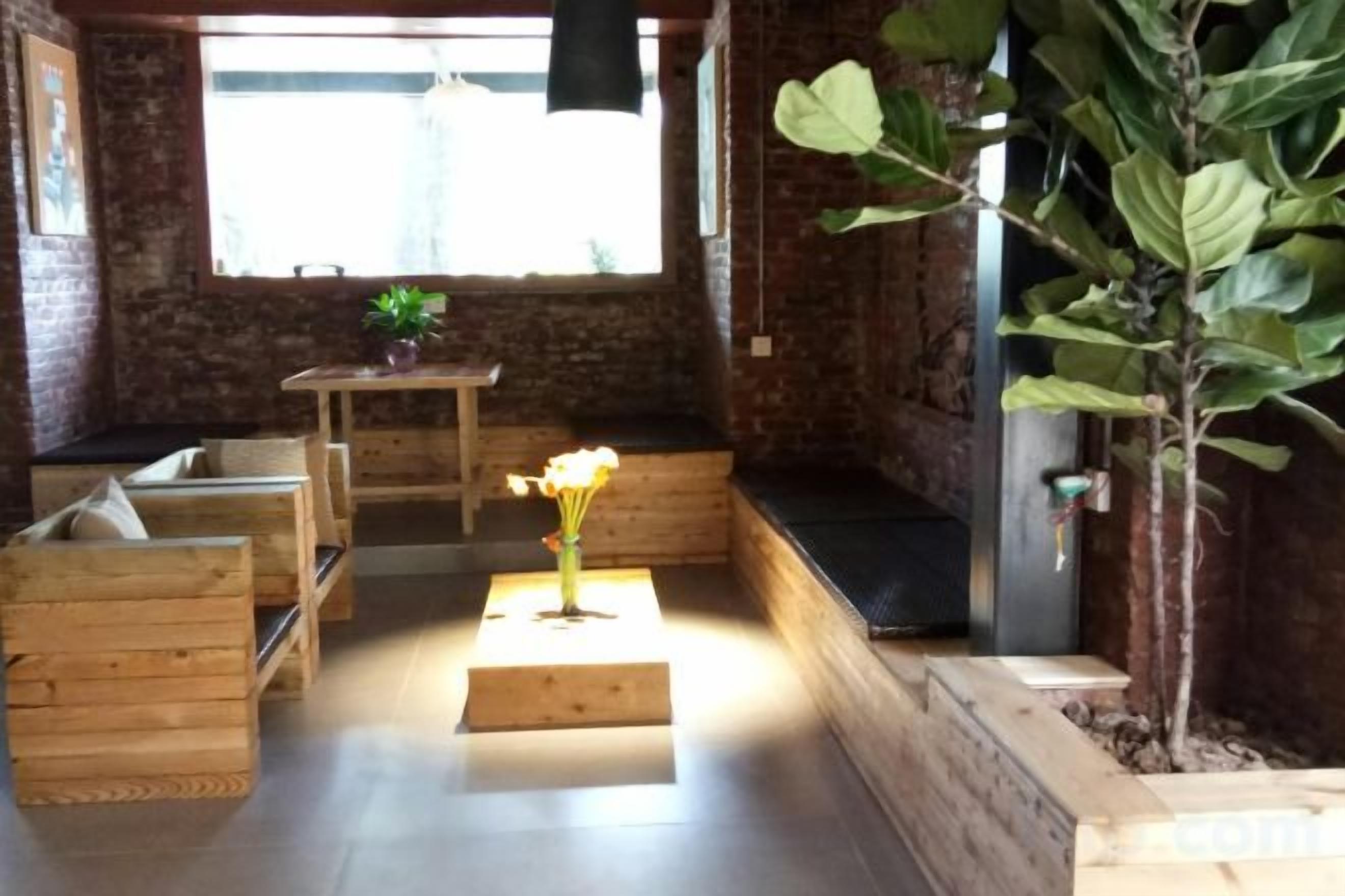 A cozy seating area with wooden benches and a small table, a potted plant, and a large window providing natural light.