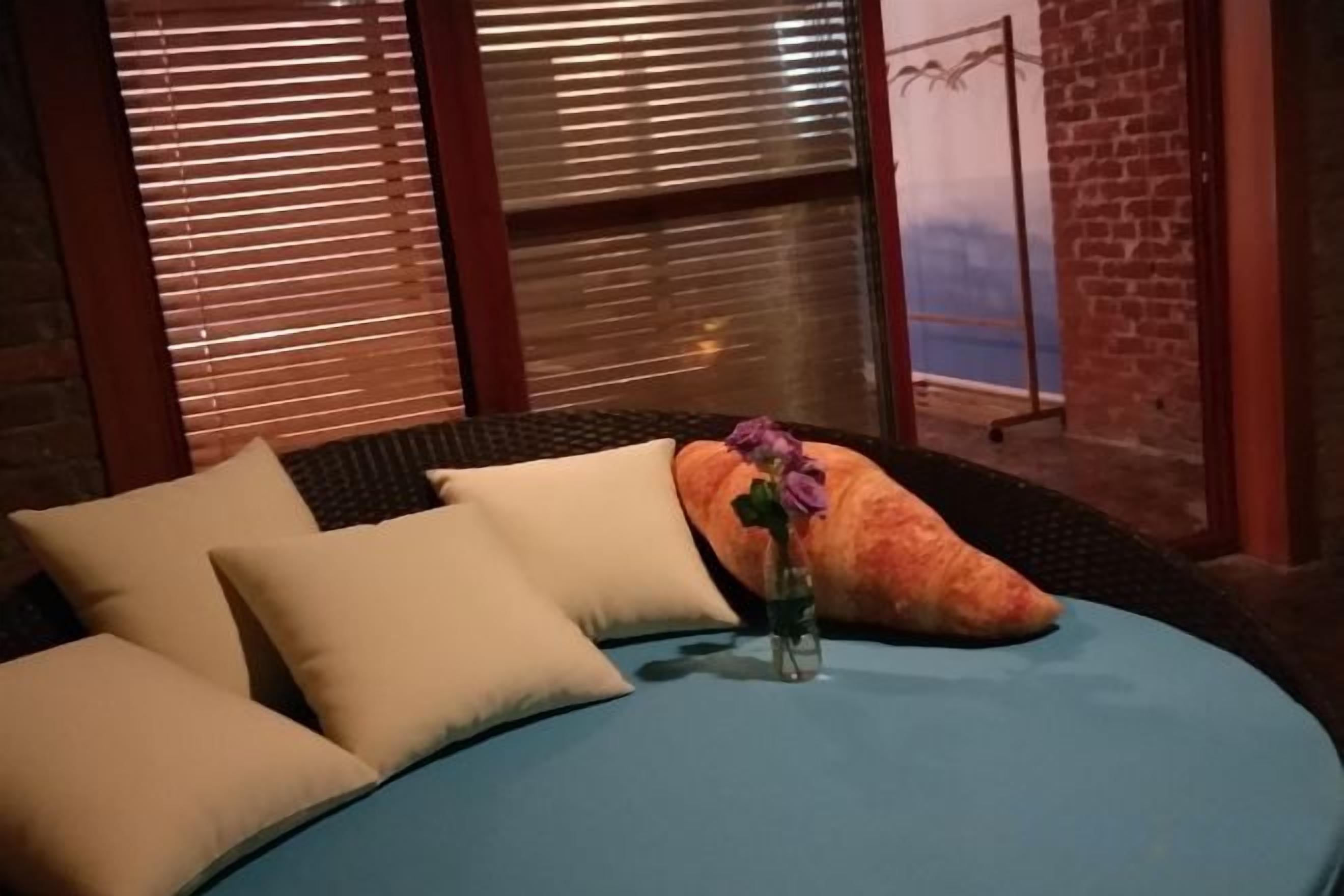 A bed with pillows and a vase with a flower, a brick wall, and a window with blinds.
