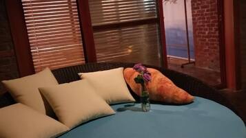A bed with pillows and a vase with a flower, a brick wall, and a window with blinds.