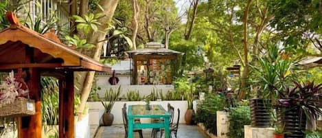 Un jardín con una mesa, sillas, un porche y diversas plantas.
