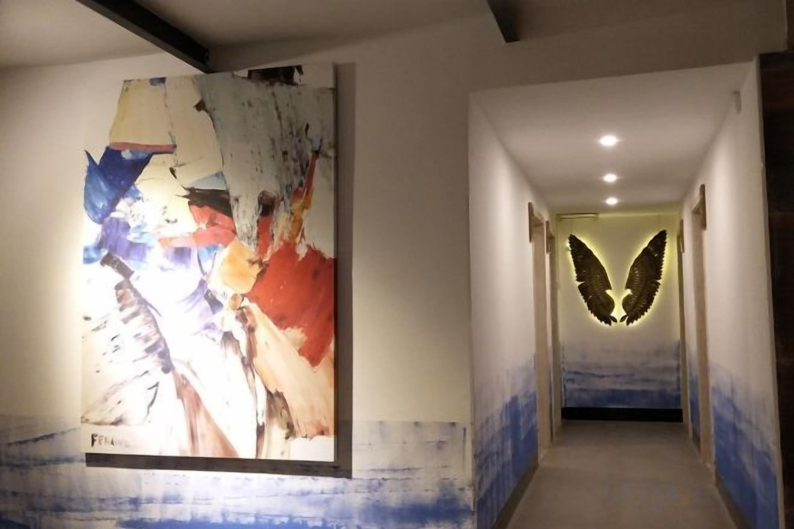 A hallway with a large abstract painting on the left and a wall-mounted illuminated design on the right.