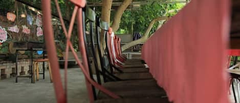 Una hilera de sillas de madera bajo un porche con mantel rosa.