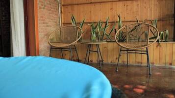A room with a bed, two wicker chairs, and a small table with a vase of plants.