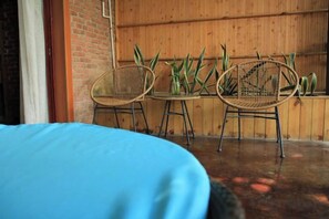 Une pièce comprenant un lit, deux fauteuils en osier et une petite table sur laquelle est posé un vase avec des plantes.