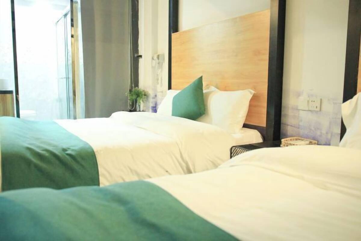 A hotel room with two beds, a wooden headboard, a small plant, and a window.