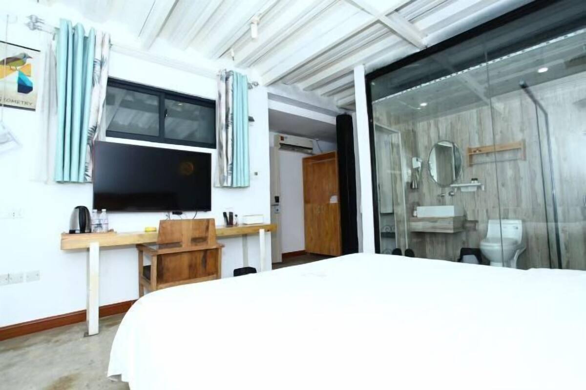 A bedroom with a bed, a TV, a desk, and a shower area.