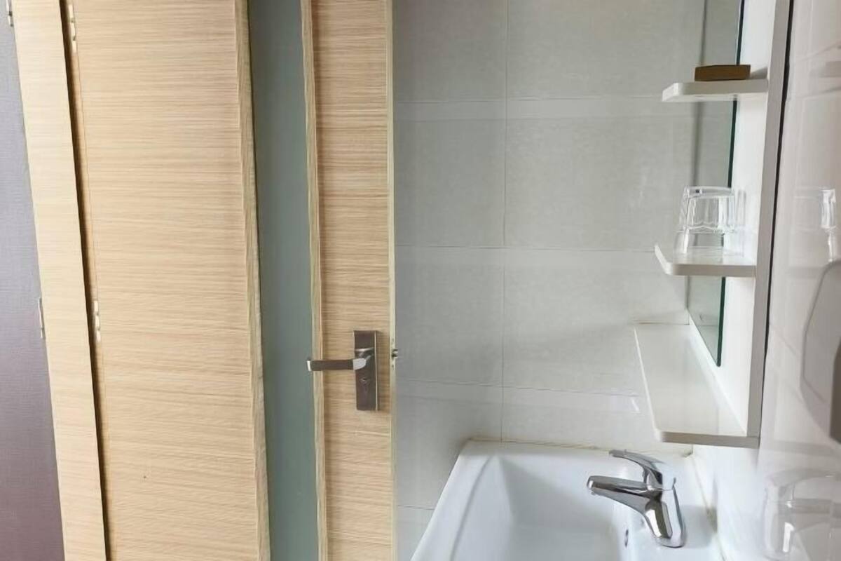 Un bany amb un rentapins blanc, un mirall i una porta de fusta.