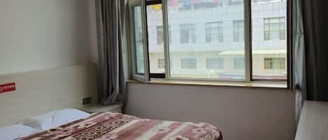 A hotel room with a bed, a window, and a view of buildings outside.