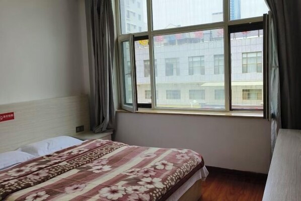 A hotel room with a bed, a window, and a view of buildings outside.