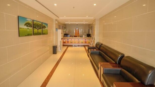 A hotel lobby with a reception desk, a waiting area with leather seating, and a corridor with tiled walls and framed artwork.