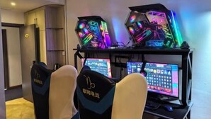 A gaming setup with two illuminated PCs and a monitor, two gaming chairs, and a desk with a keyboard and mouse.