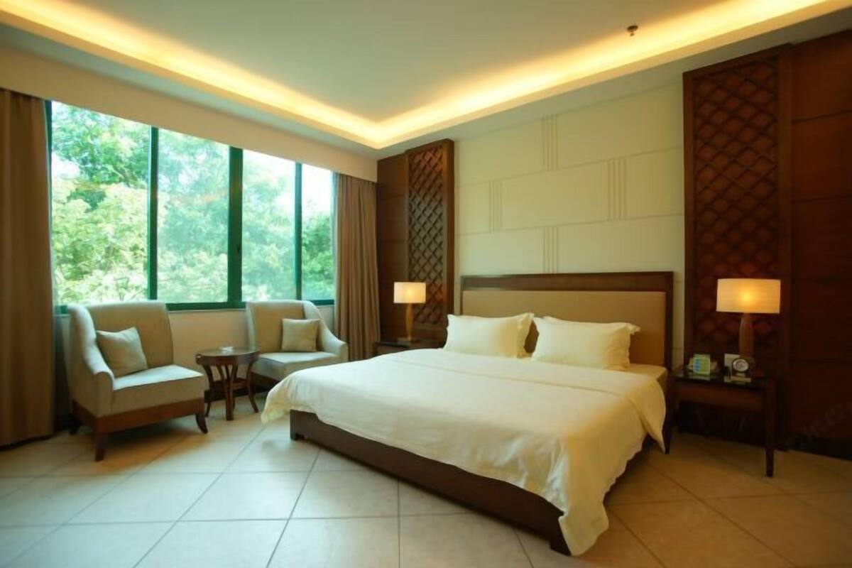 A hotel room with a large bed, two bedside tables, a chair, and a window with curtains.