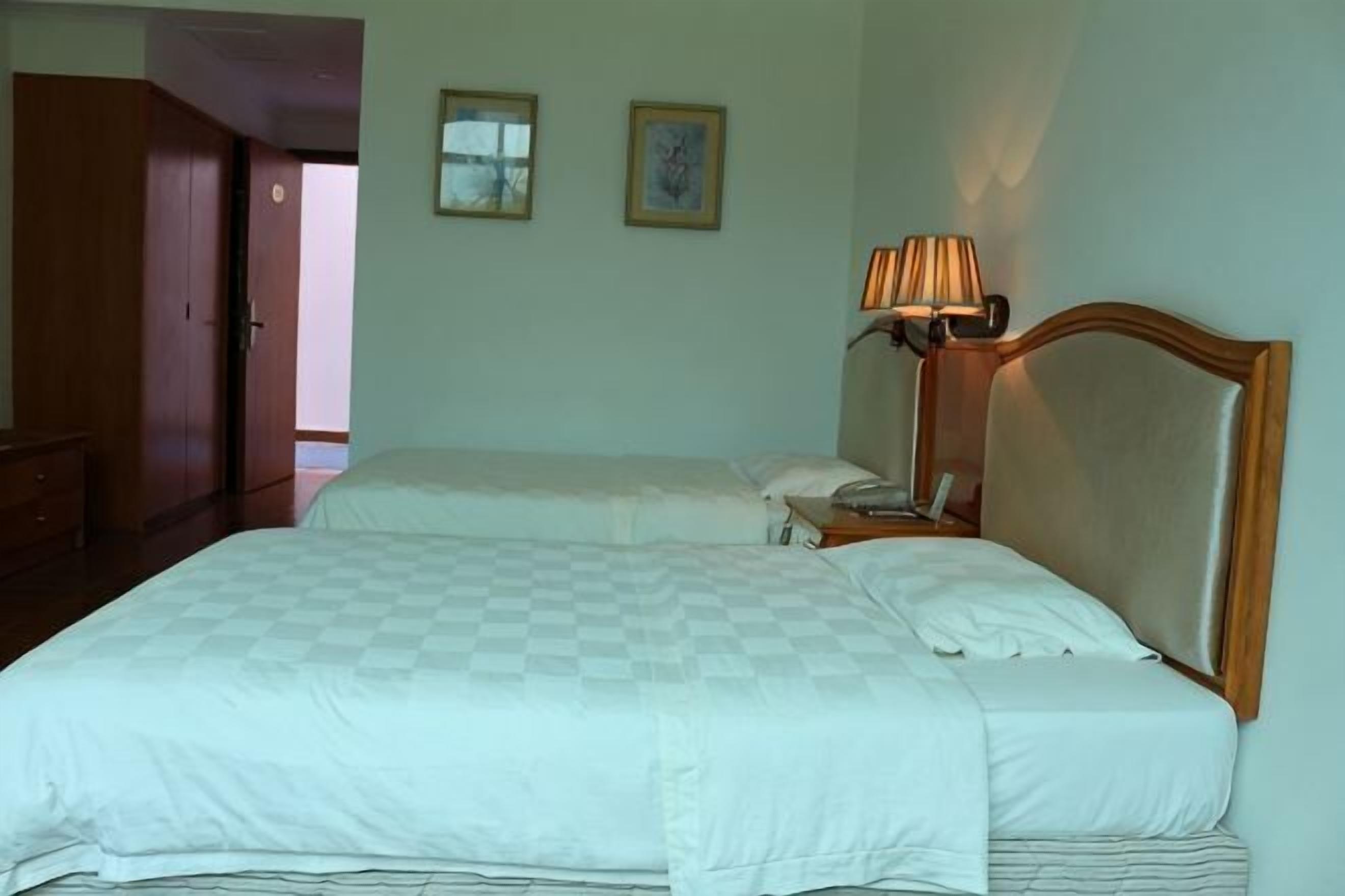 Uma cama de casal com colcha xadrez, abajur e cabeceira de madeira.