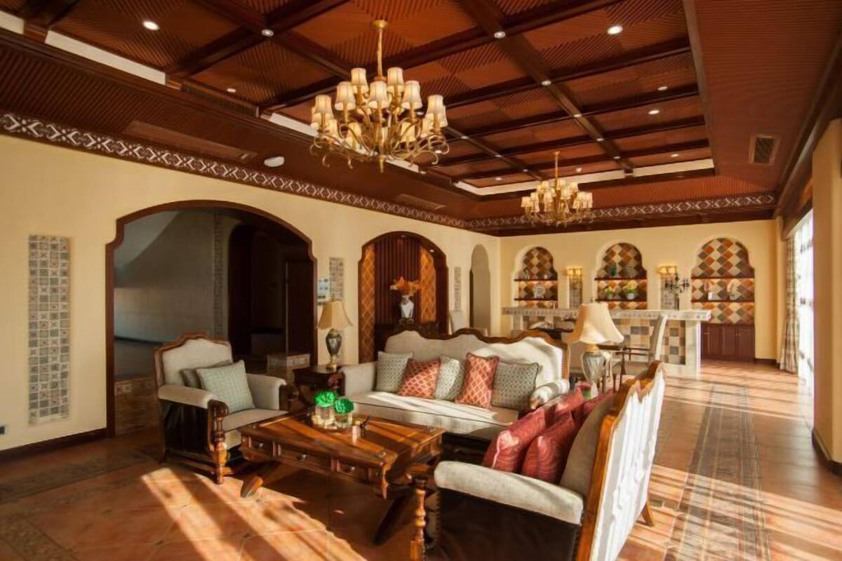A spacious living room with a high ceiling, ornate chandeliers, and a checkered floor.