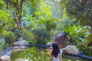 A person sitting by a pond surrounded by lush greenery.
