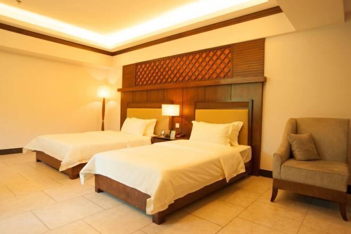 A hotel room with two beds, a nightstand, a lamp, and a chair.