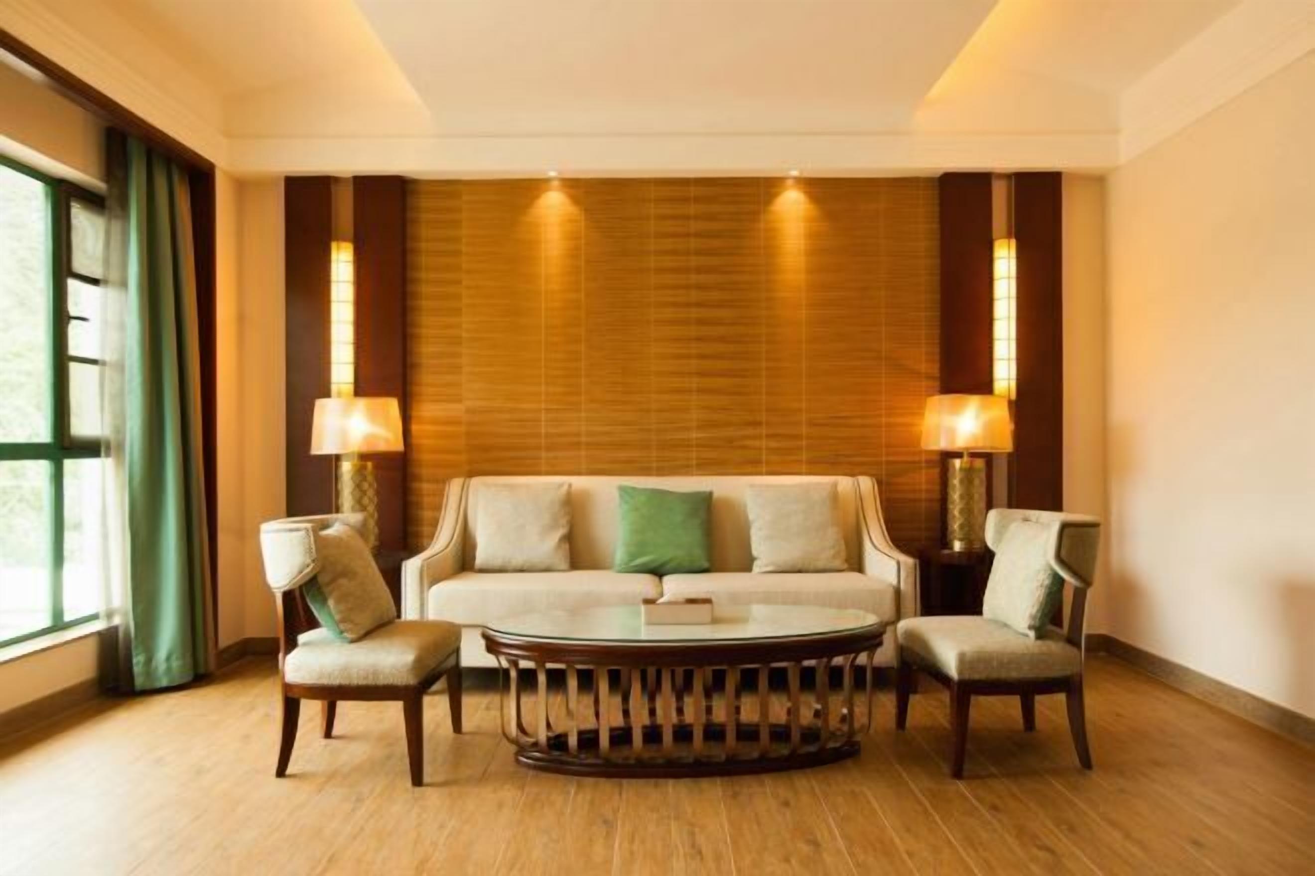 Una habitación con un sofá, dos sillones, una mesa redonda de centro y dos lámparas.