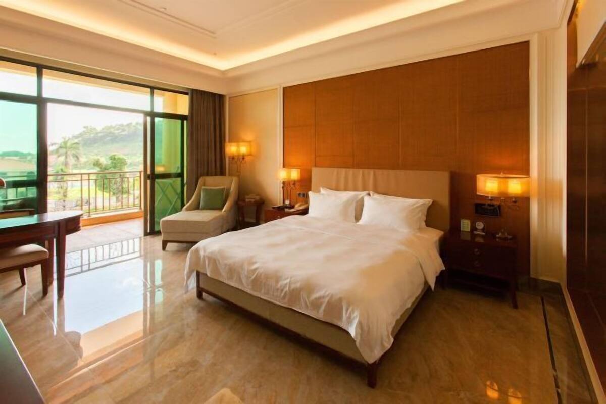 A hotel room with a large bed, two bedside tables, a chair, a desk, and a balcony with a view.