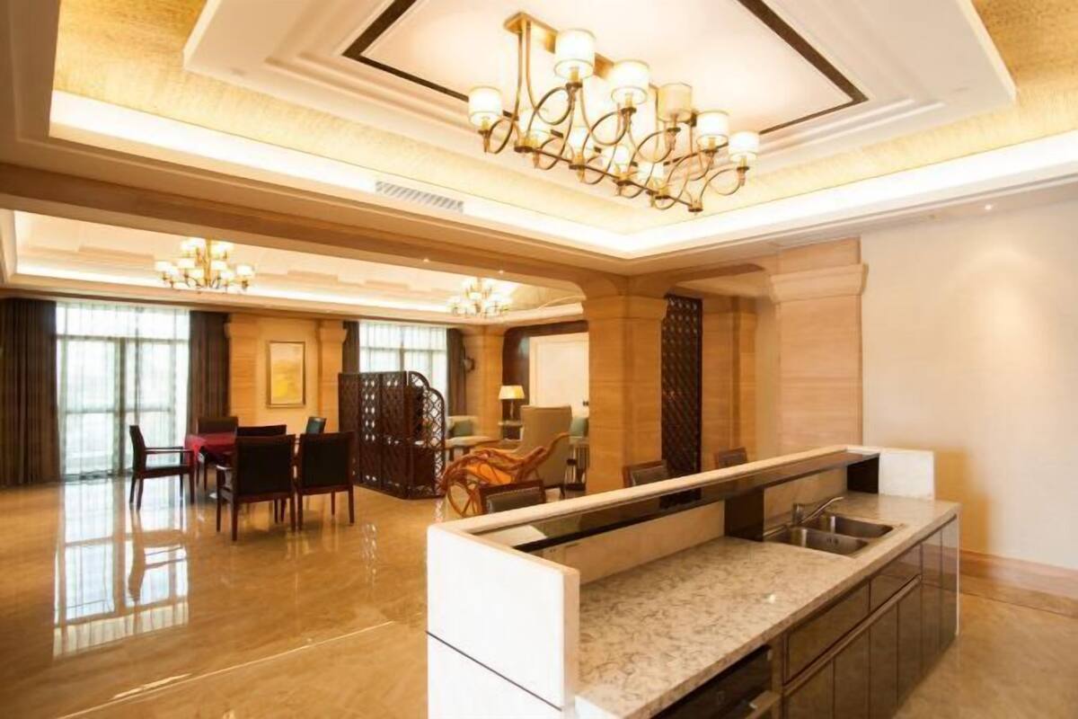 A spacious hotel lobby with a marble reception desk, multiple seating areas, and elegant chandeliers.