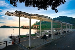 A waterfront outdoor seating area with a covered structure, tables, and chairs. - Hubin Hotel (Foshan)