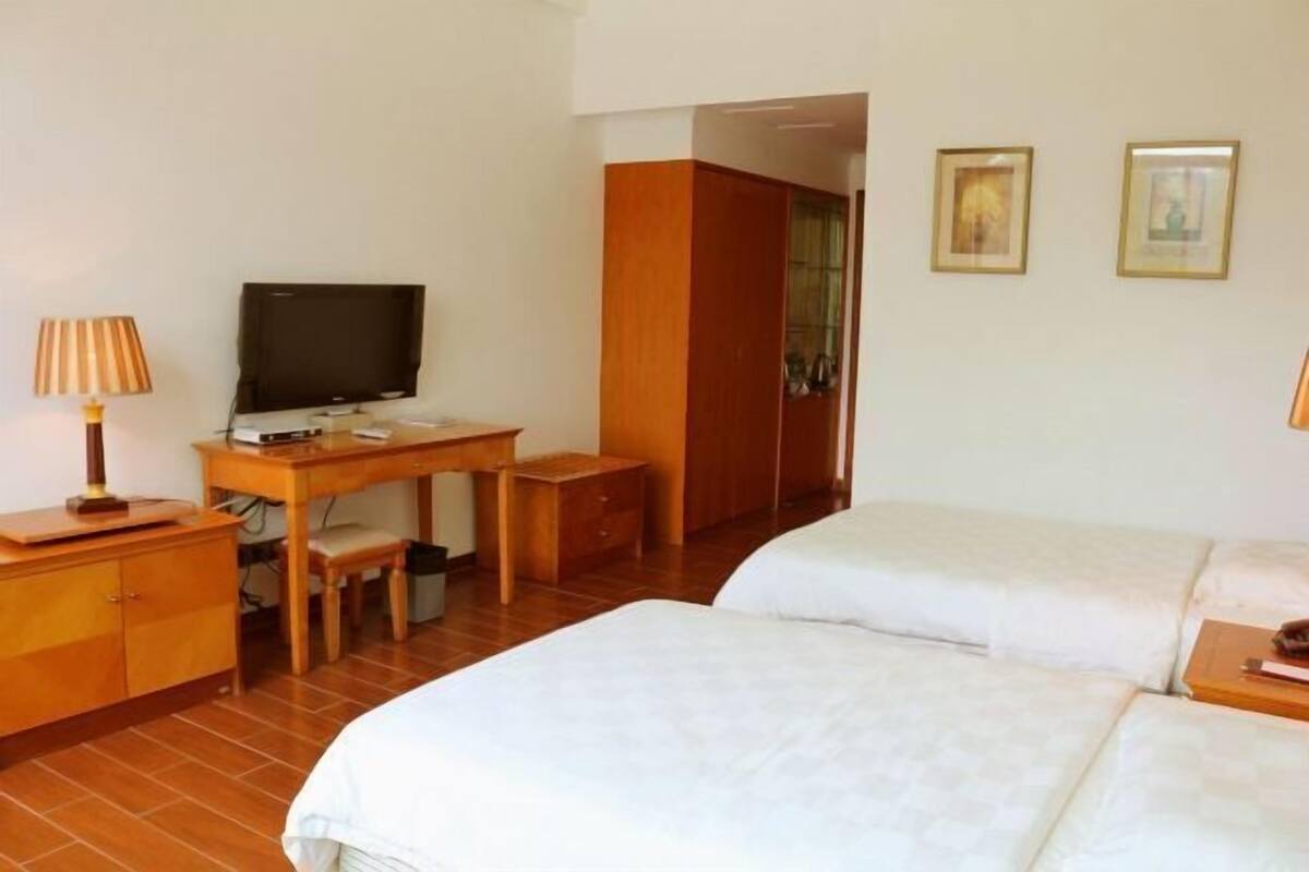 A hotel room with a bed, a desk with a television, a lamp, and a wardrobe.