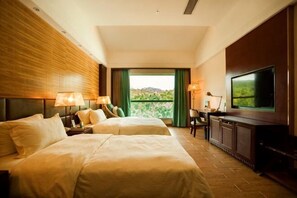 Ein Hotelzimmer mit zwei Betten, einem Fernseher, einem Schreibtisch und Blick auf Grünflächen.