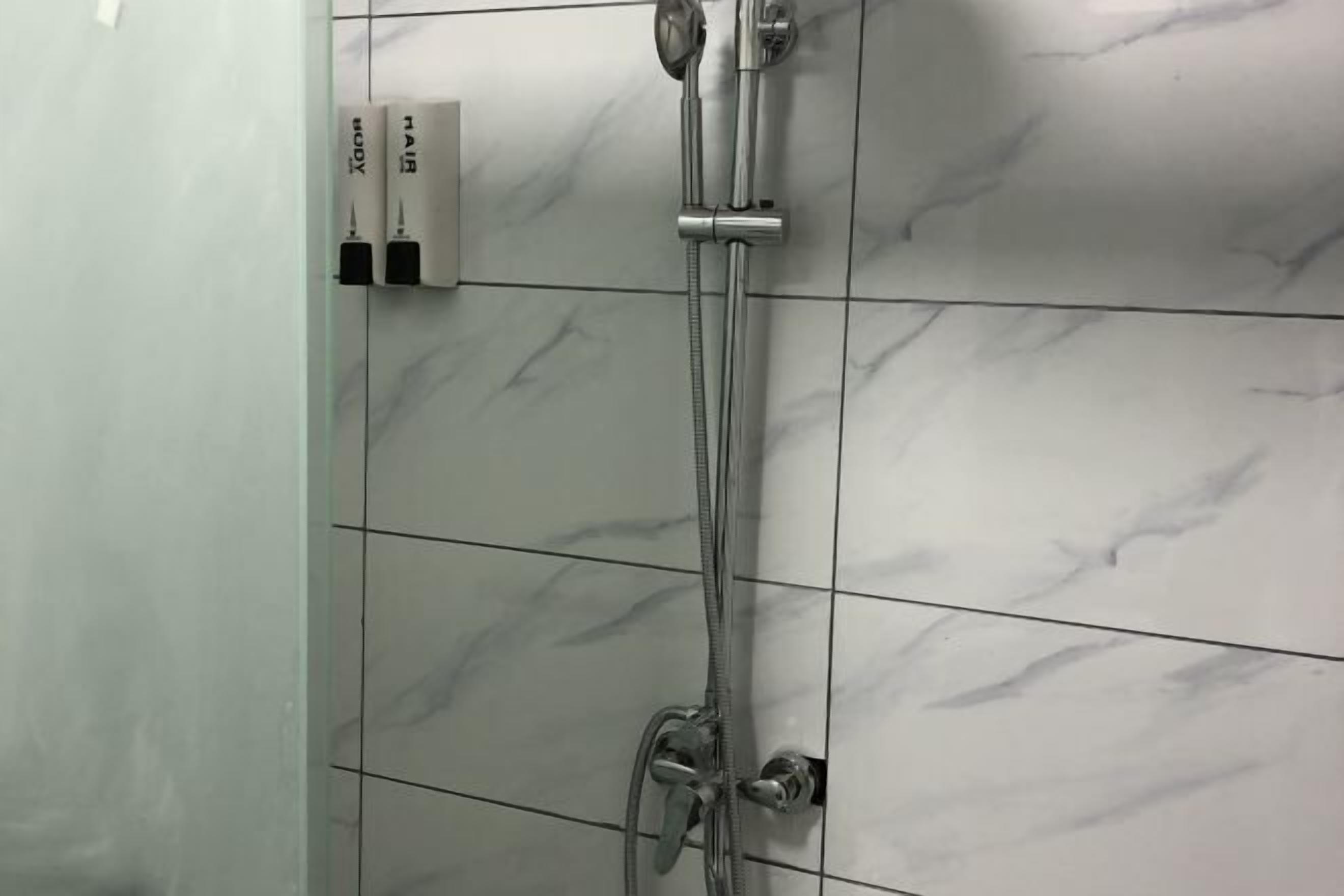 A bathroom with a shower, tiled walls, and a soap dispenser.