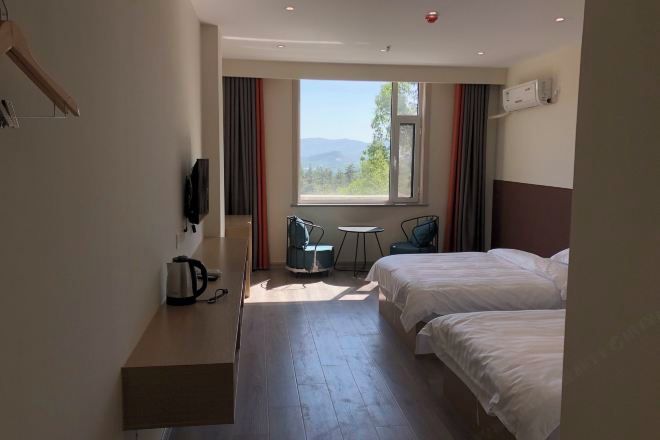 Quarto de hotel com duas camas, uma mesinha, uma cadeira, televisão e janela com vista.