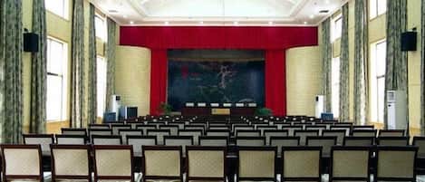 A conference room with rows of chairs facing a stage with a red curtain backdrop.