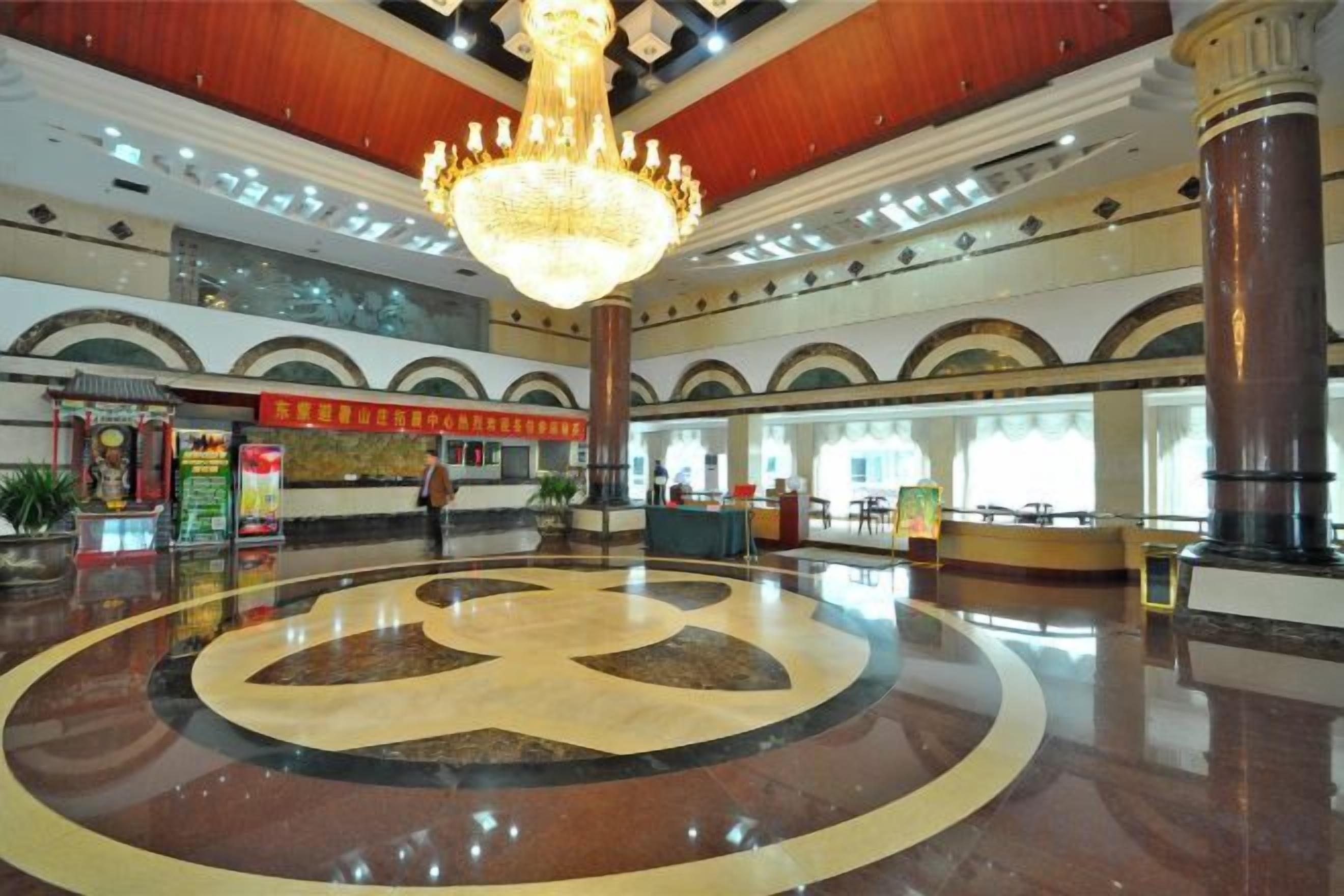A spacious lobby with a central circular design, a grand chandelier, and a reception area.