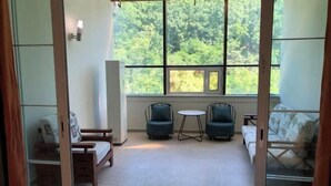 Ein Zimmer mit einem großen Fenster, zwei blauen Sesseln, einem kleinen runden Tisch und einem Sofa.