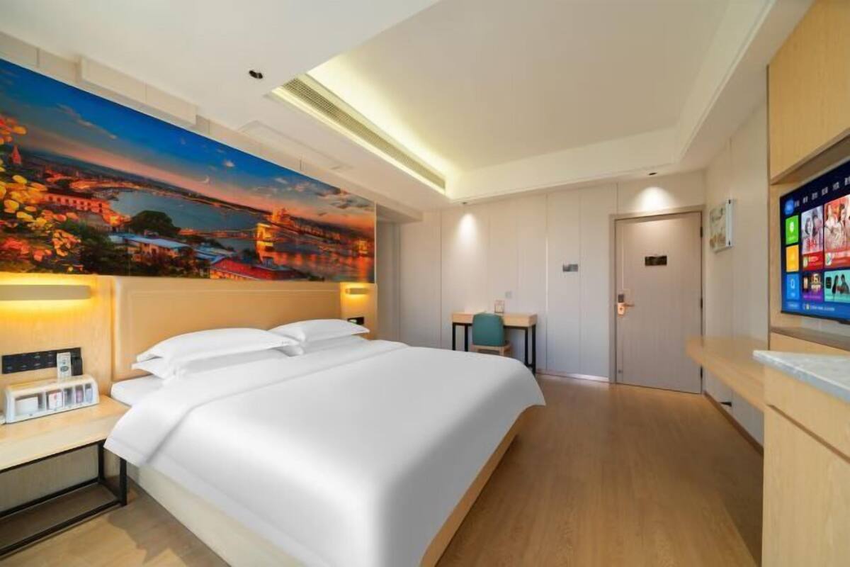 A hotel room with a bed, a desk, a chair, a TV, and a painting on the wall.