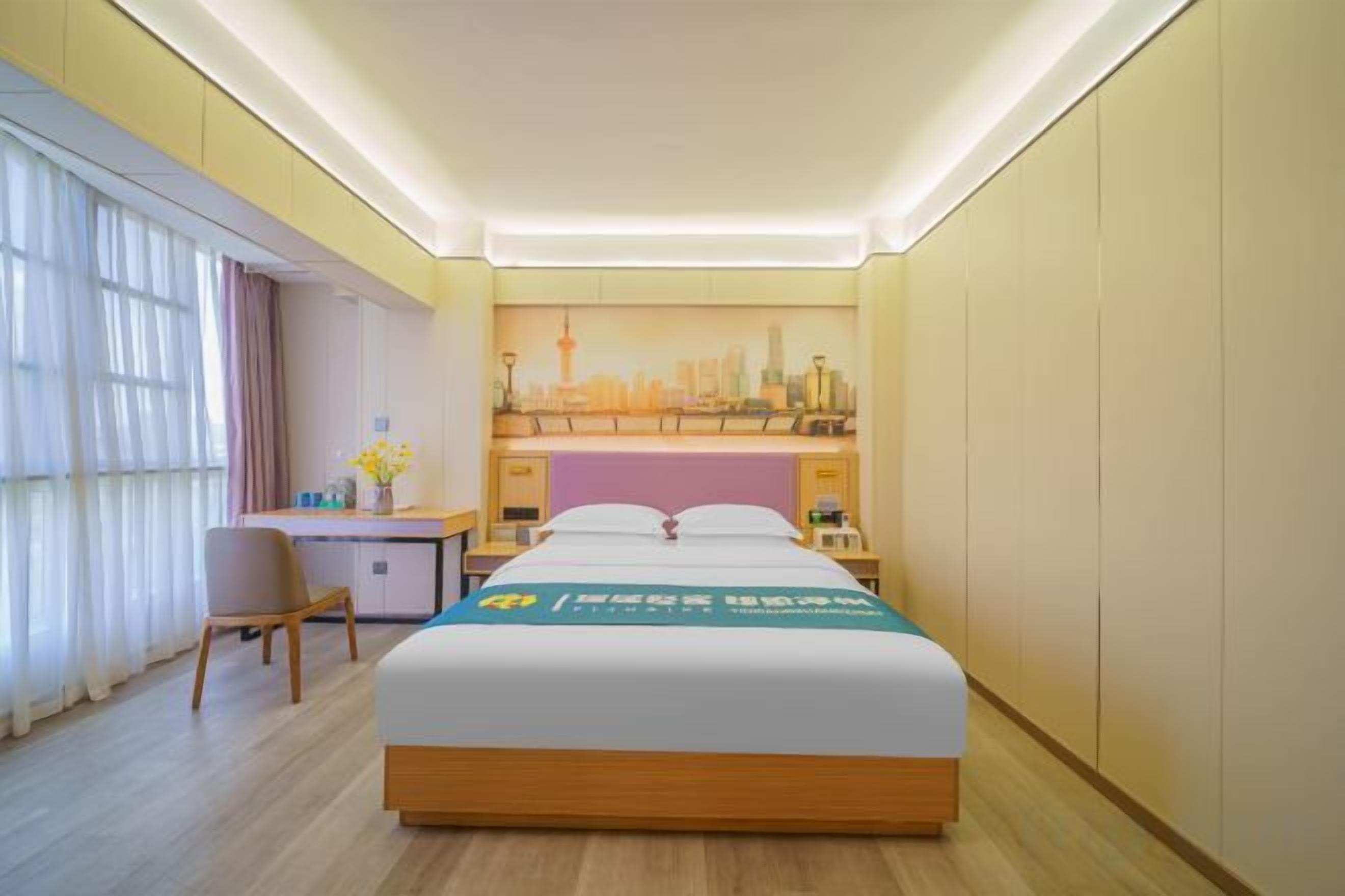 Habitación de hotel con cama, escritorio, silla y un cuadro de un paisaje urbano en la pared.